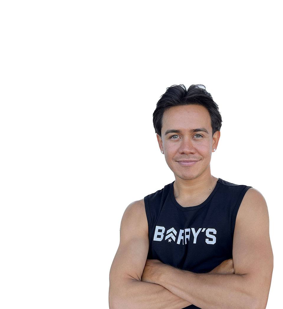 Barry's instructor standing confidently with arms crossed in front, wearing a black tank top against a white background, ready for the next workout challenge.
