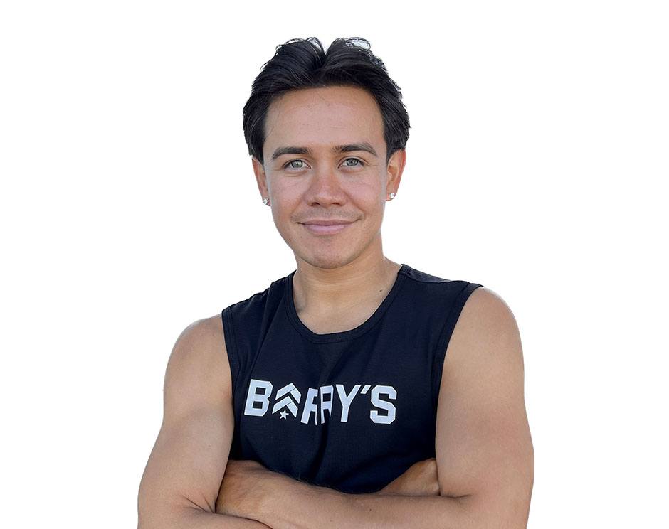 Barry's instructor standing confidently with arms crossed in front, wearing a black tank top against a white background, ready for the next workout challenge.