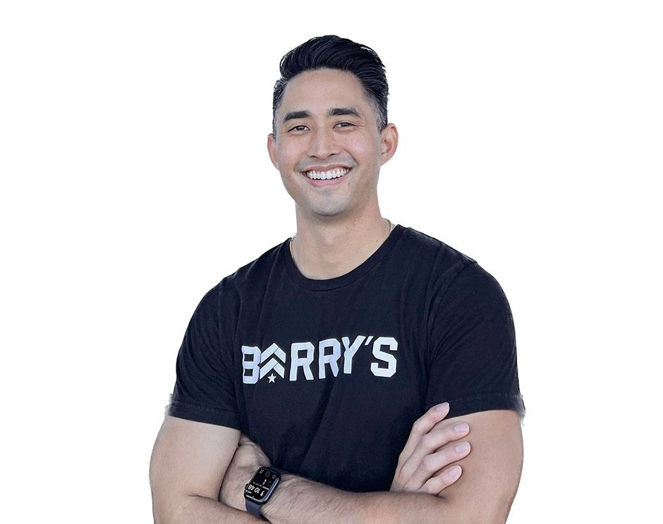 Barry's instructor standing confidently with arms crossed in front, wearing a black tank top against a white background, ready for the next workout challenge.