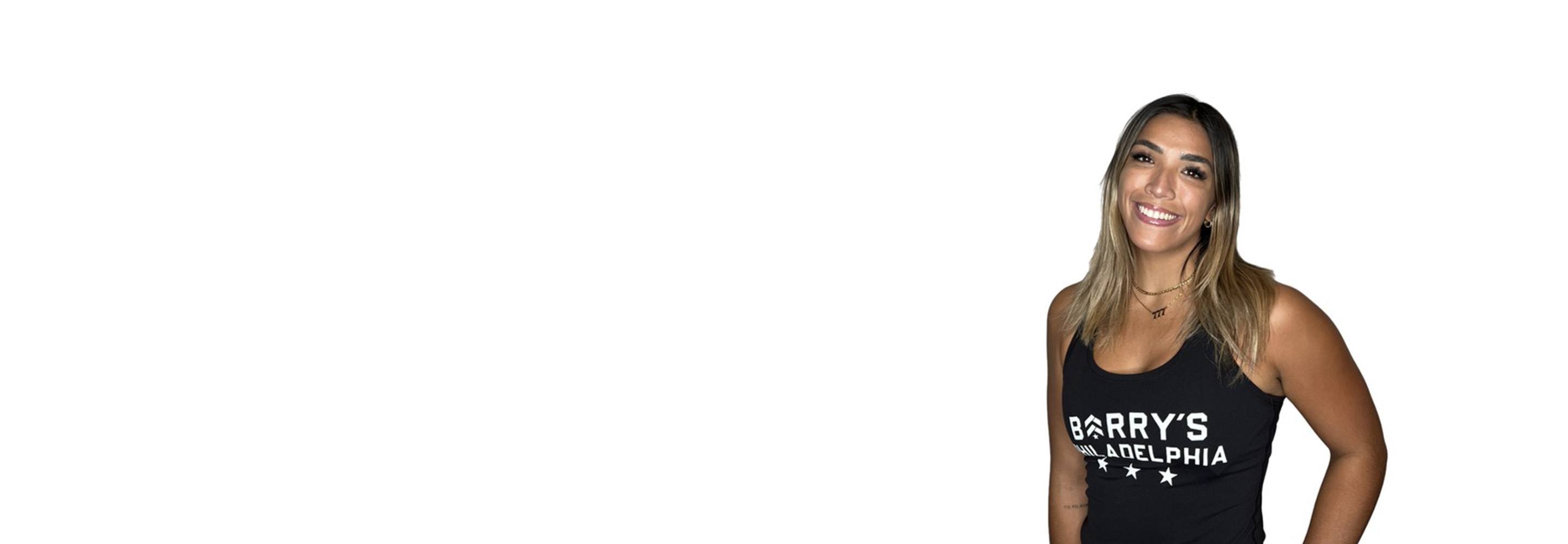 Barry’s instructor wearing a black top standing confidently smiling against a white background