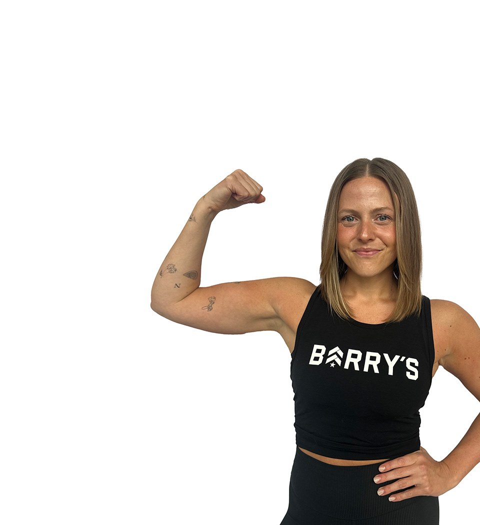 Barry’s instructor wearing a black top standing confidently smiling against a white background