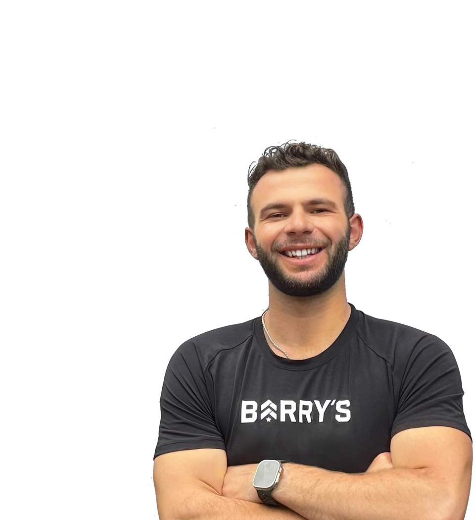 Barry's instructor standing confidently wearing a black tank top against a white background, ready for the next workout challenge.