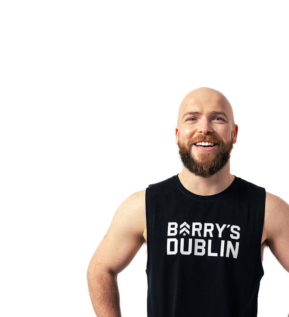 Barry’s instructor wearing a black top standing confidently smiling against a white background