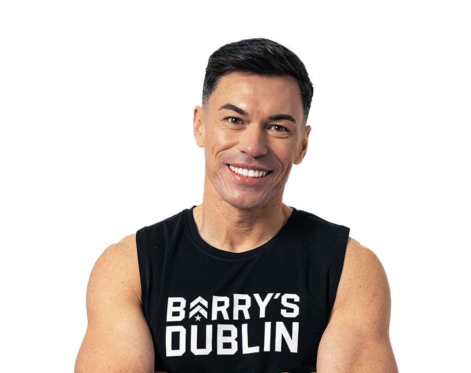 Barry’s instructor wearing a black top standing confidently smiling against a white background