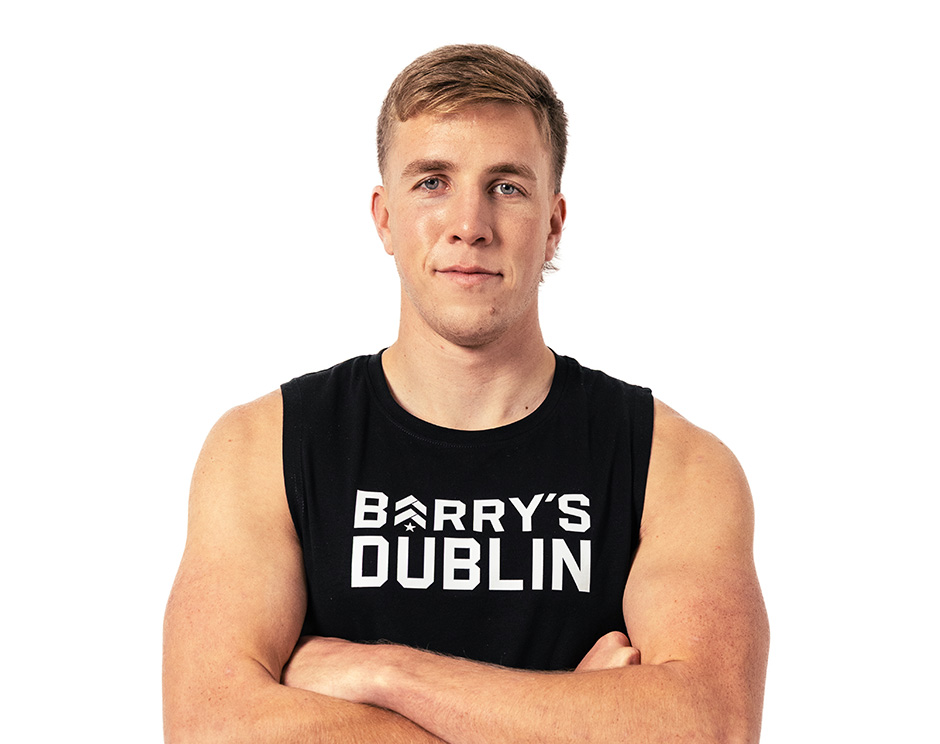 Barry’s instructor wearing a black top standing confidently smiling against a white background